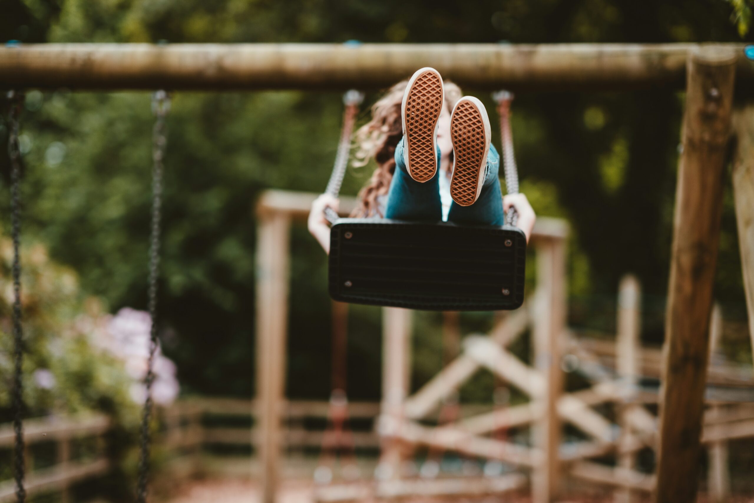 Photo of young person on a swing viewing soles of trainers as they fly high.